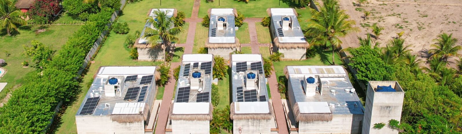 A hotel with multiple buildings featuring solar panels on the roofs, surrounded by lush greenery and palm trees.