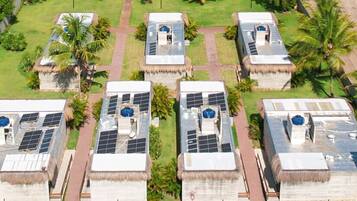 A hotel with multiple buildings featuring solar panels on the roofs, surrounded by lush greenery and palm trees.