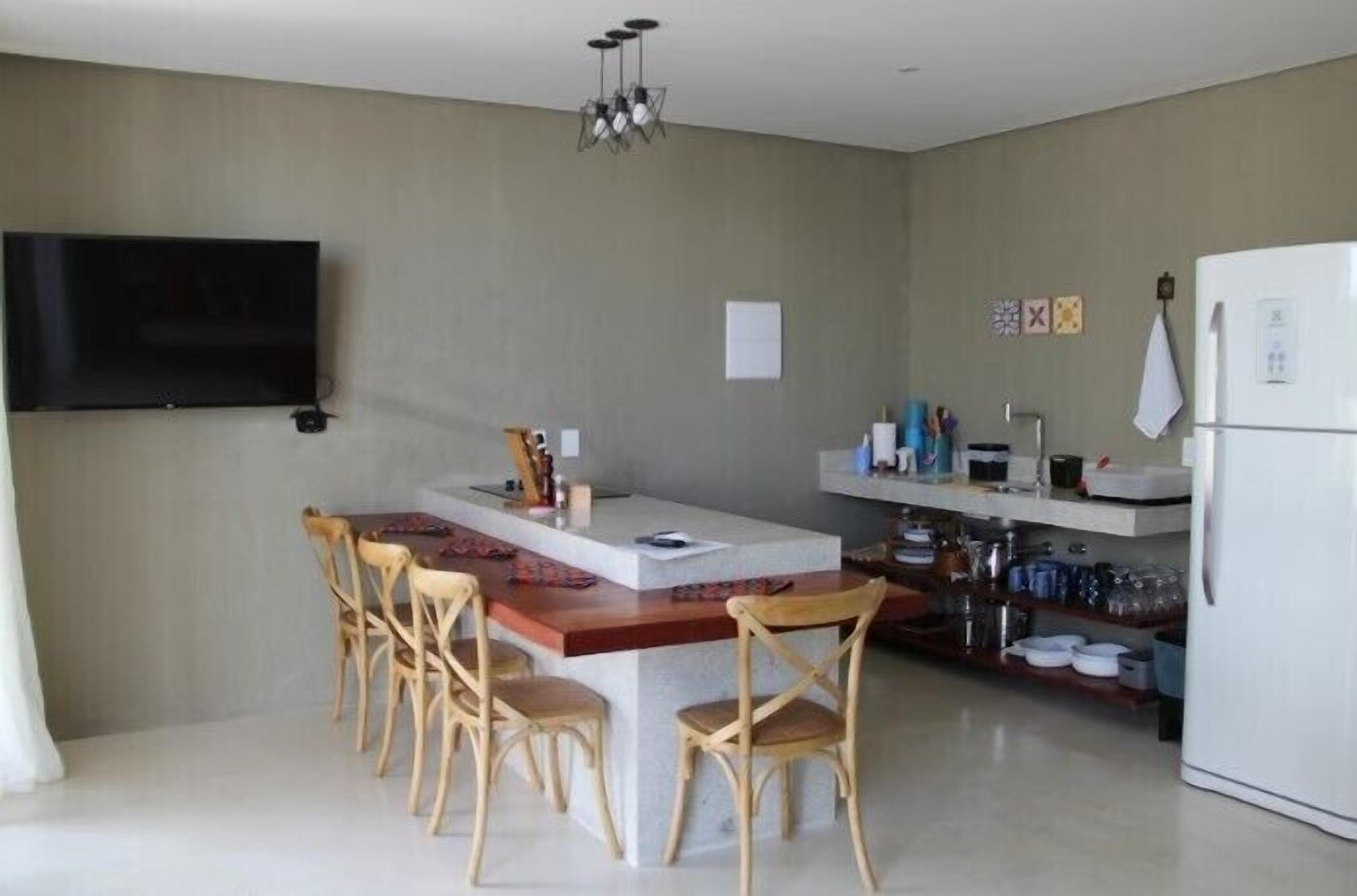 Una cocina moderna con una isla central, sillas de madera, un televisor de pantalla plana y un refrigerador blanco.