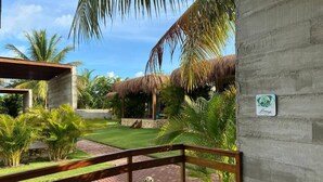A concrete building with a wooden railing, a grassy area, and a thatched-roof structure.