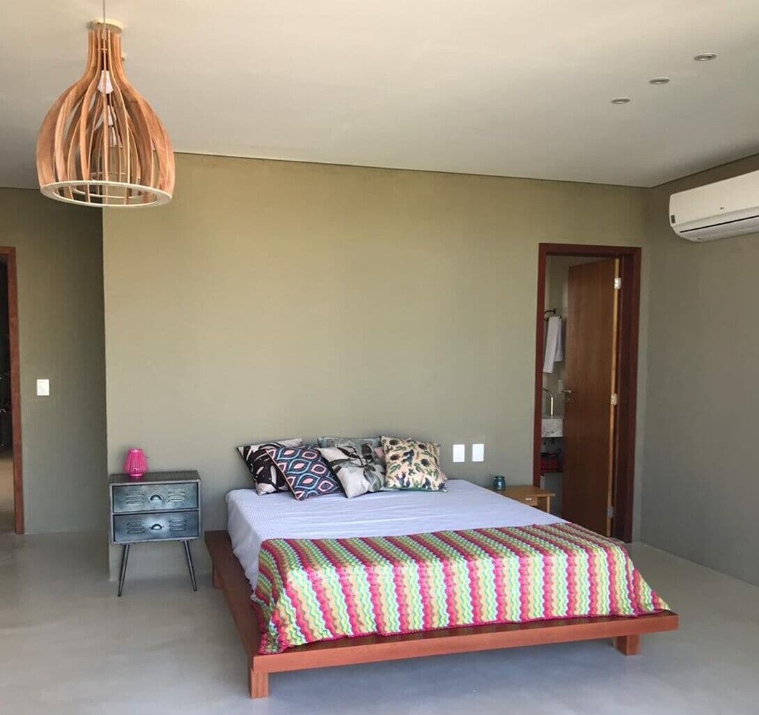 A bedroom with a bed, bedside tables, a hanging light fixture, and an air conditioning unit.