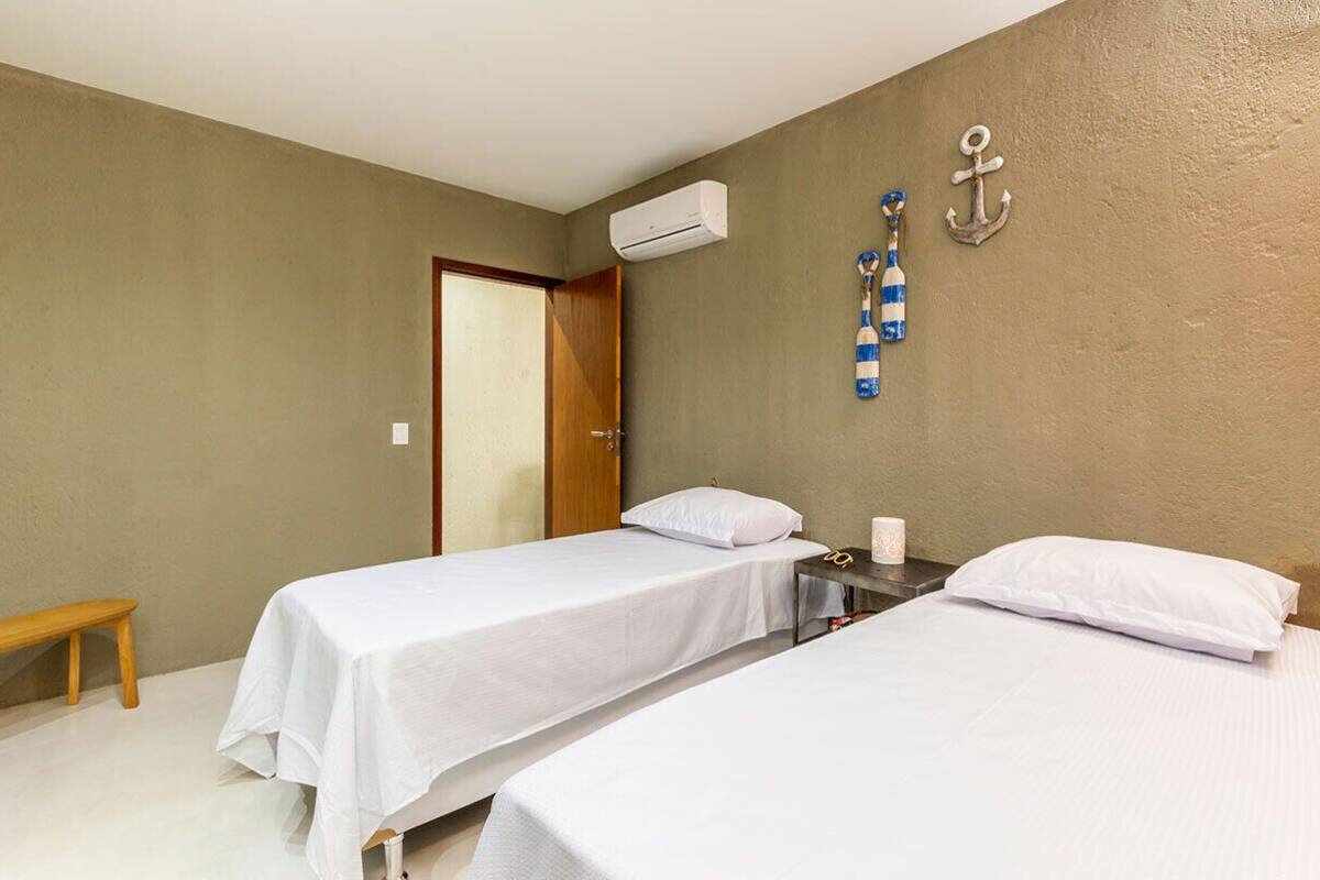 Une chambre avec deux lits simples, un banc en bois, un appareil de climatisation et une porte.