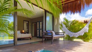 A modern pool area with a hammock, a sofa, and a bed visible through glass doors.