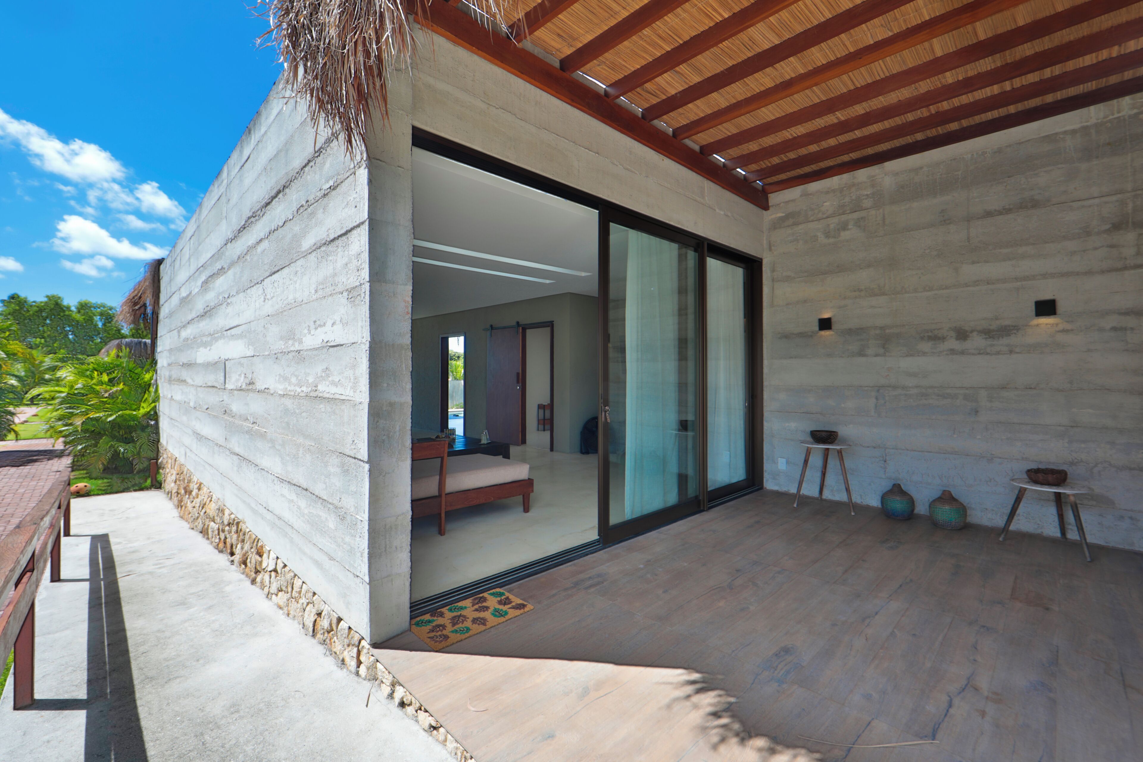 A modern house with a patio, a dining area, and a bedroom visible through glass doors.