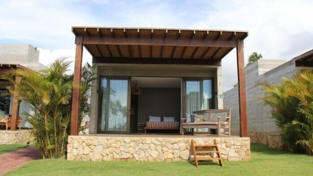 A modern outdoor lounge area with a stone base, wooden furniture, and a pergola.