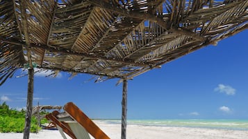 Relax in a beachside haven with a comfortable chair under a shaded roof.