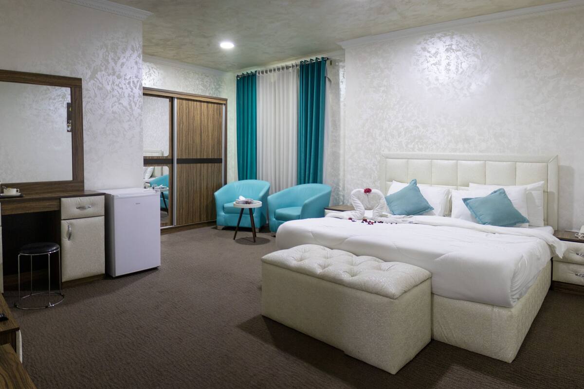 A hotel room with a bed, a desk with a computer, a chair, a small table, and a wardrobe.