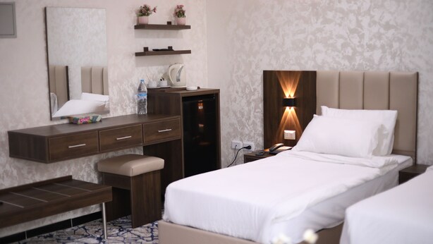 A hotel room with a bed, bedside table, lamp, and a desk with a chair. - The Castle hotel (Amman)