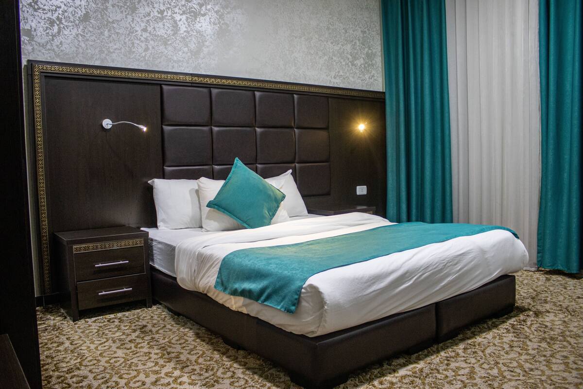A neatly made bed with a headboard, a bedside table with drawers, and a wall-mounted light.