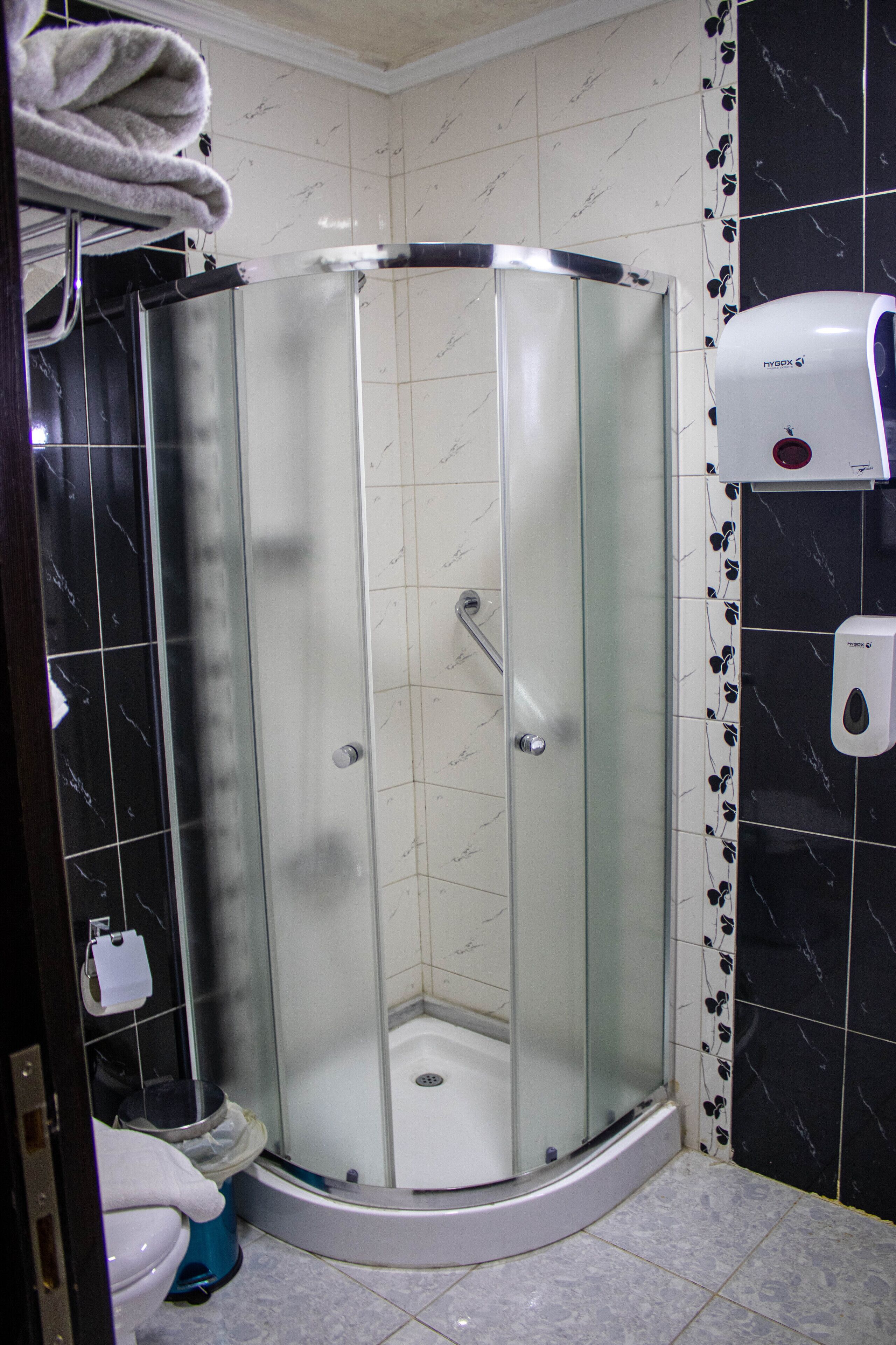 A corner shower with a glass door, a hand dryer, and a toilet with a towel hanging on the wall.