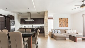 Una cocina moderna con armarios oscuros, una zona de comedor con mesa y sillas, y una sala de estar con sofá y una mesa de centro.