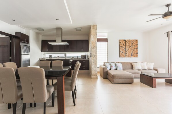 A modern kitchen with dark cabinets, a dining area with a table and chairs, and a living room with a sofa and a coffee table. - Costa Hermosa C302LO_200Mpbs_Pool_BBQ_Walk to the Beach (Bavaro-Punta Cana)