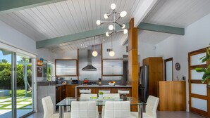 Una cocina moderna con electrodomésticos de acero inoxidable, una mesa de comedor de vidrio con sillas blancas y un amplio ventanal con vistas a un jardín.