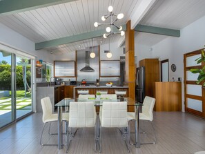A modern kitchen with stainless steel appliances, a glass dining table with white chairs, and a large window overlooking a garden.