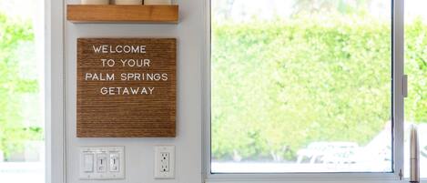 A kitchen with a window, a welcome sign, and a shelf with colorful containers.