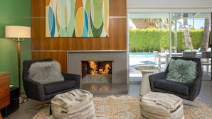 Una sala de estar moderna con chimenea, dos sillones, una alfombra y vistas a una piscina.