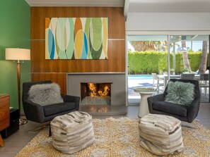 A modern living room with a fireplace, two armchairs, a rug, and a view of a pool.
