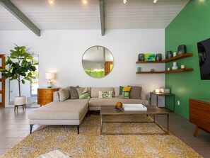 Un salon moderne avec un canapé d’angle, une table basse, un miroir rond et un mur d’accent vert.