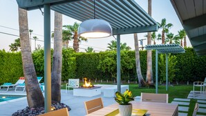 Un patio al aire libre con mesa y sillas de madera, una chimenea y una pérgola.