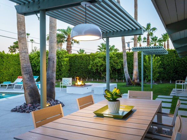 Une terrasse extérieure avec une table en bois, des chaises, un foyer et une pergola.