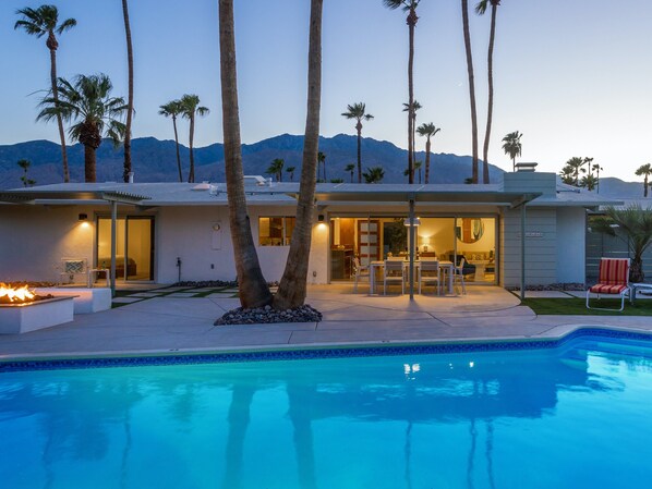 A modern house with a swimming pool, palm trees, and a mountain backdrop.