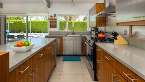 Una cocina moderna con electrodomésticos de acero inoxidable, armarios de madera y un amplio ventanal con vistas a una piscina y vegetación.