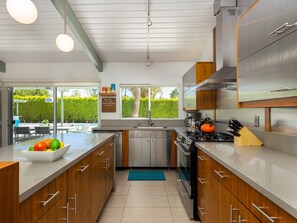 A modern kitchen with stainless steel appliances, wooden cabinets, and a large window offering a view of a pool and greenery.