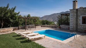 A swimming pool with lounge chairs, a pergola, stone walls, and a stone chimney. - Koules Estate-Anemone, with Pool & BBQ, an Agricultural barn for Nature lovers (Rethymno)