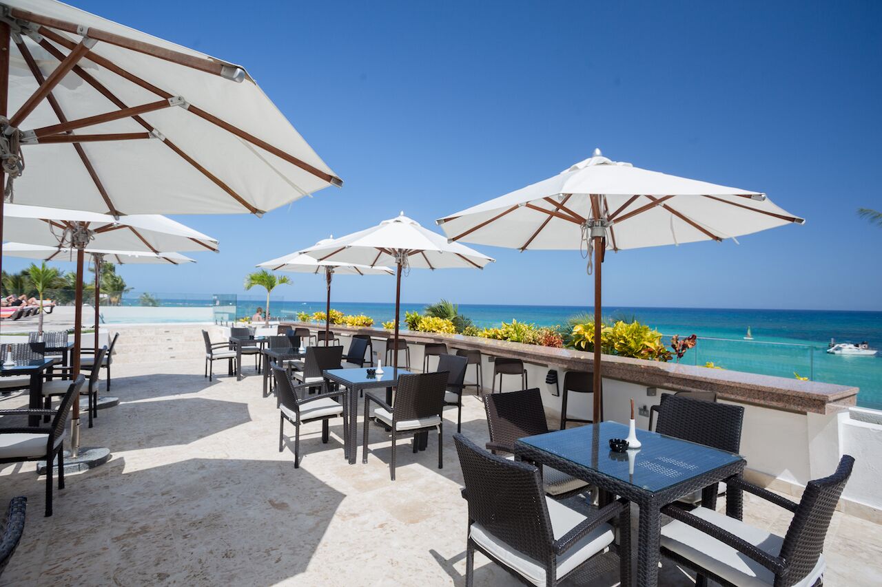 A beachside outdoor seating area with white umbrellas, wicker furniture, and a view of the ocean.