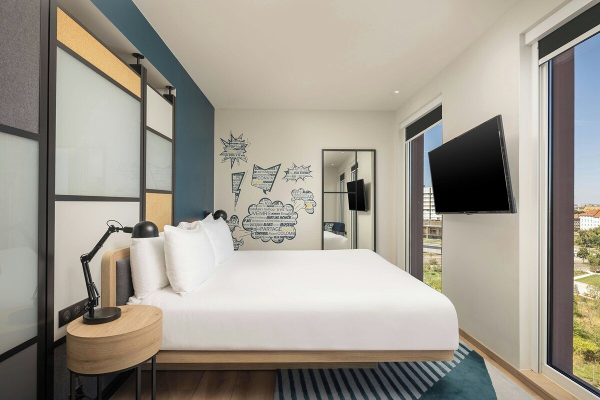 A modern bedroom with a bed, bedside table, lamp, and a wall with text and graphics.