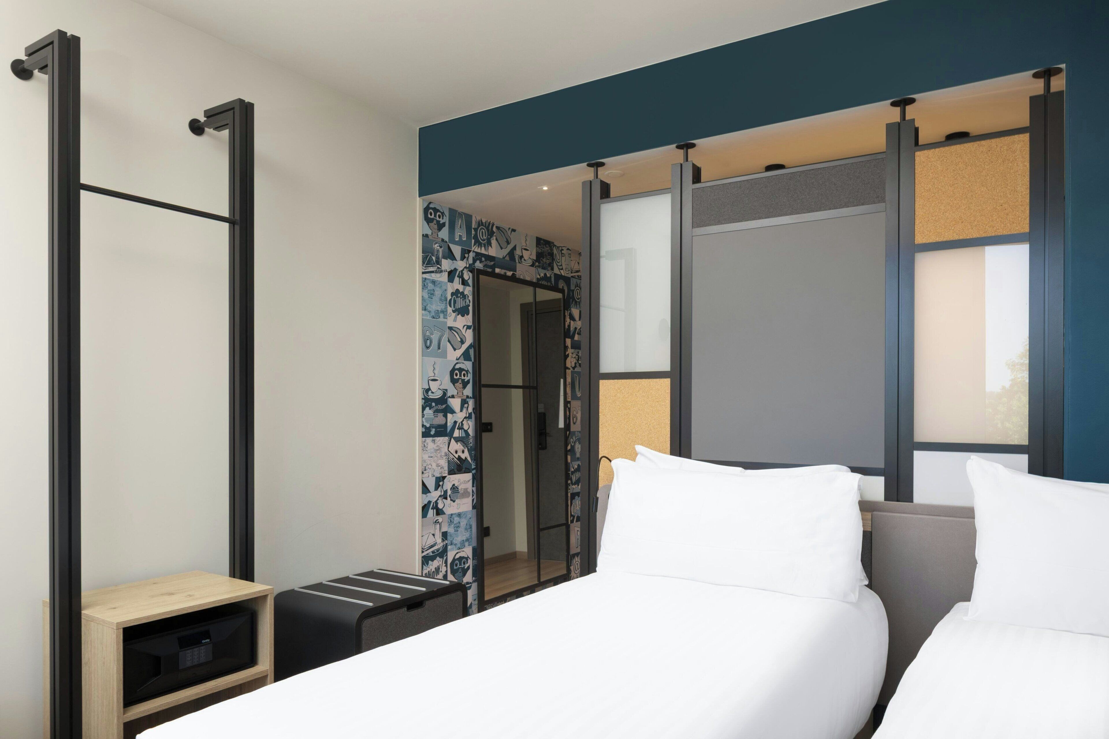 Habitación de hotel con cama, una mesita de noche de madera, escritorio extraíble, un espejo grande y una puerta corrediza que da al baño.