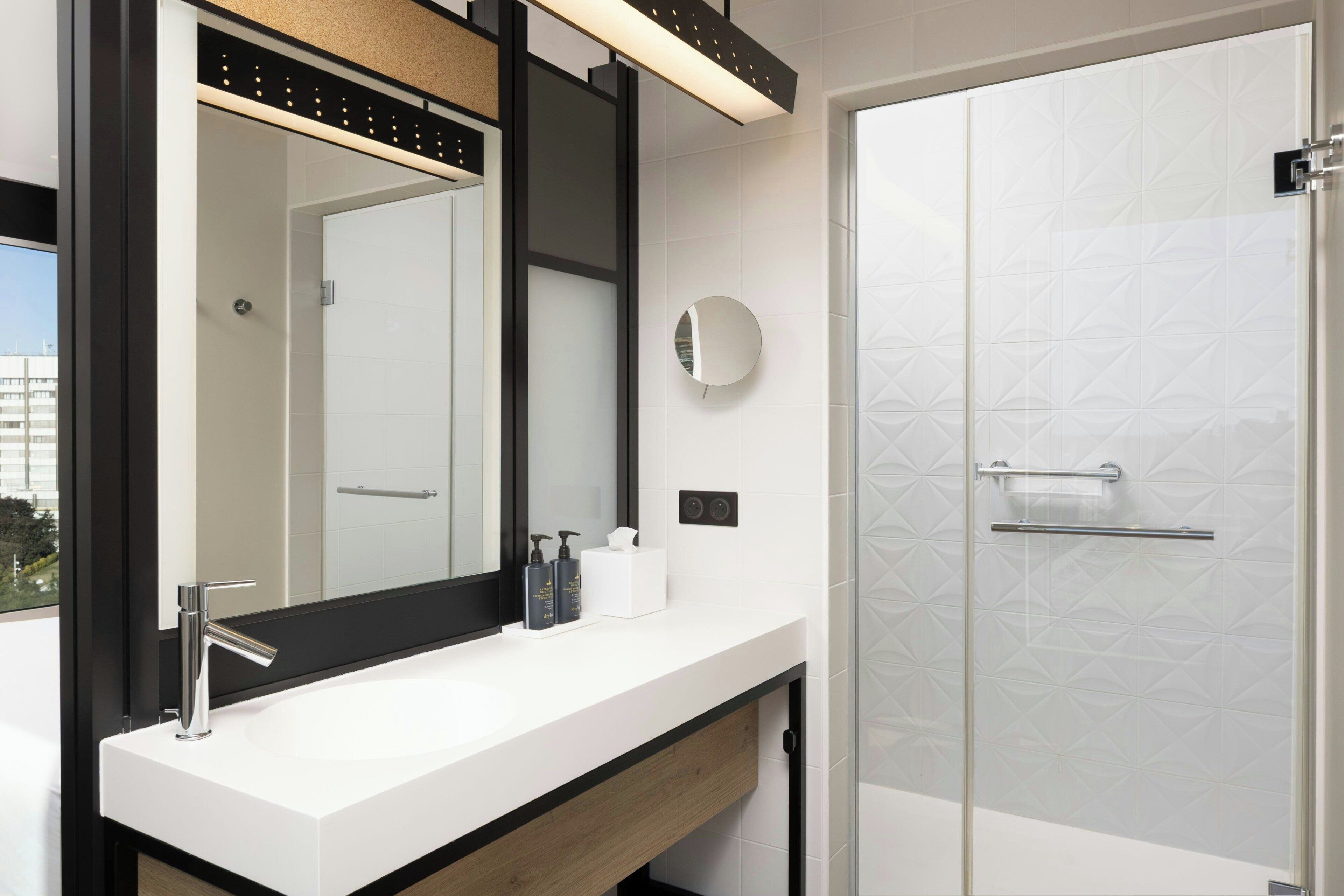 A modern bathroom with a large mirror, a white sink, a glass shower enclosure, and a towel rack.