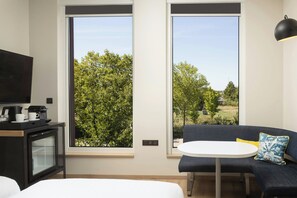 A modern room with a sofa, a small table, a TV, and a coffee machine. - Aloft by Marriott Strasbourg City Centre (Strasbourg)