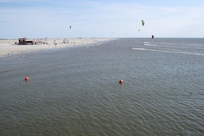 Una playa con una torre de salvavidas, agua tranquila y varios boyas naranjas.