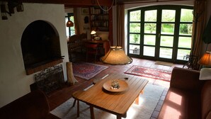 A cozy living room with a fireplace, a dining table, and a large window with a view of greenery.