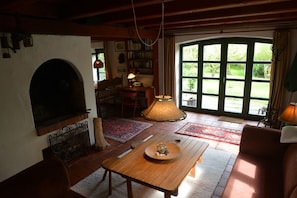 Una sala de estar acogedora con chimenea, una mesa de comedor y un ventanal con vistas a la vegetación.