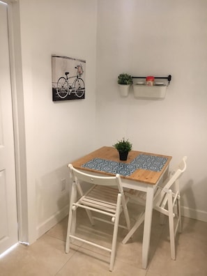 Cozy retreat with a single bed, table, and chairs, featuring a potted plant and framed artwork.