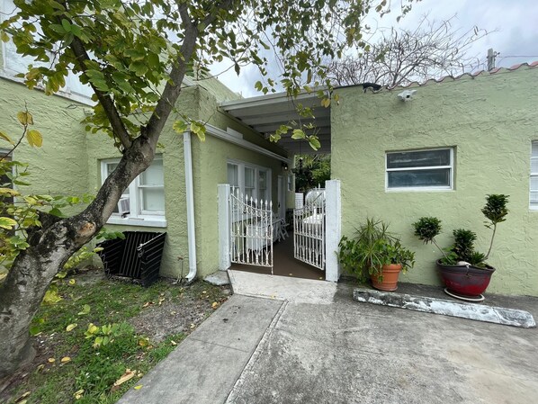 A house with a green exterior, a gated entrance, and potted plants.