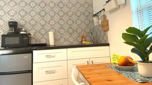 Une cuisine avec un papier peint à motifs, un four à micro-ondes, une machine à café, un évier et une table en bois sur laquelle est posée une plante en pot.