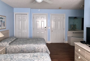 A bedroom with two beds, a dresser, a mirror, and a ceiling fan.