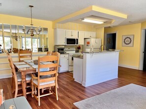 A kitchen with white cabinets, a central island, and a dining area with wooden chairs and a table. - Beautiful condo, golf course view. Close to shops, restaurants and the beach.  (Calabash)