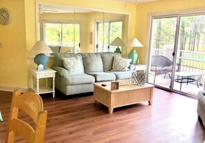 A living room with a sofa, a coffee table, and two lamps. There is a sliding glass door leading to an outdoor area.