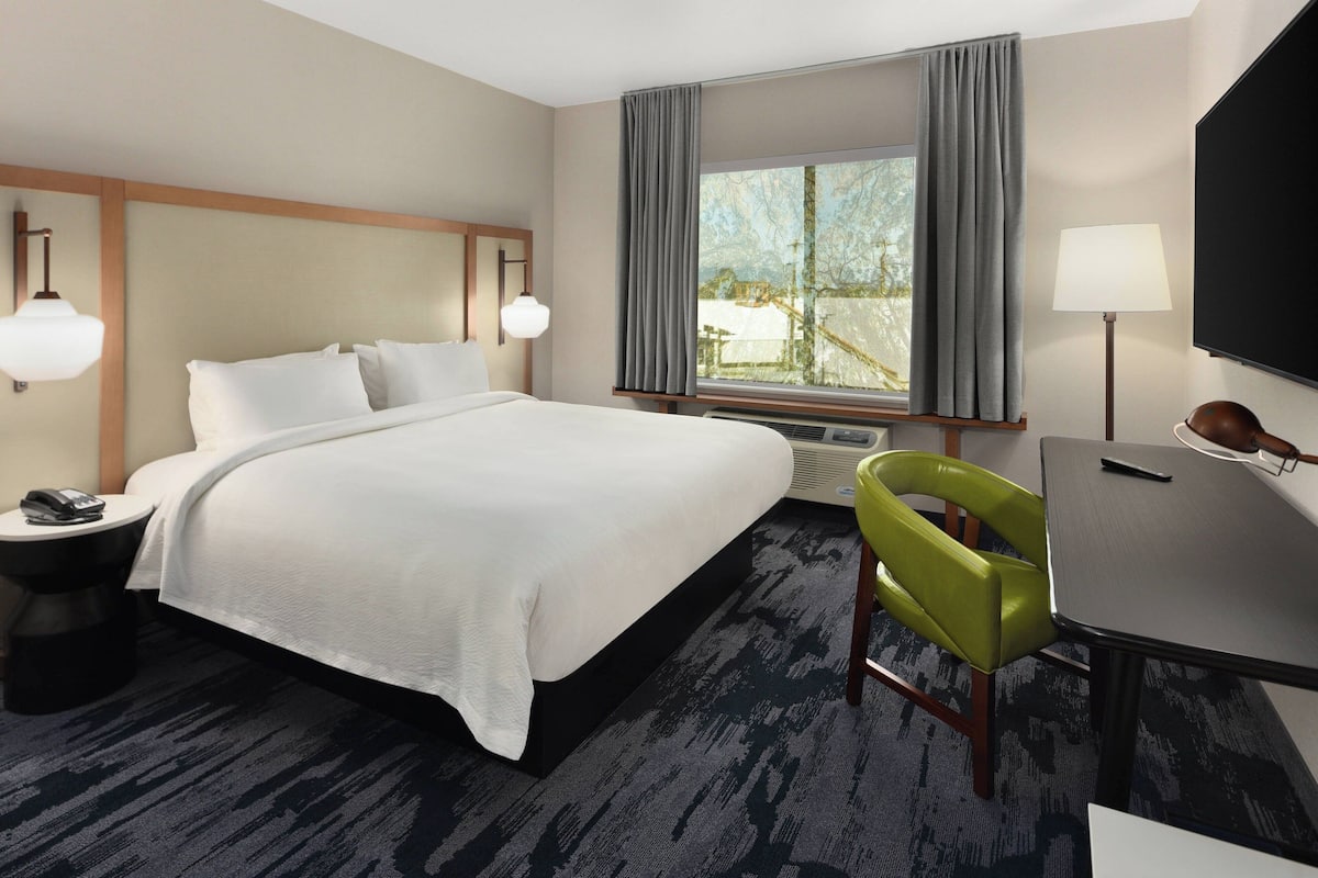 A hotel room with a large bed, a desk, a chair, a TV, and a window with curtains.