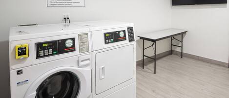 A guest laundry area with a front-loading washing machine and dryer, a table, and a sign with laundry instructions.