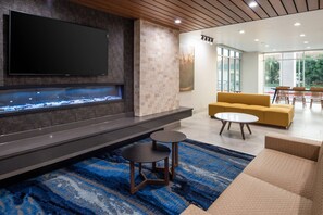 A modern living area with a flat-screen TV, a built-in fireplace, a yellow sofa, and a dining table with chairs.