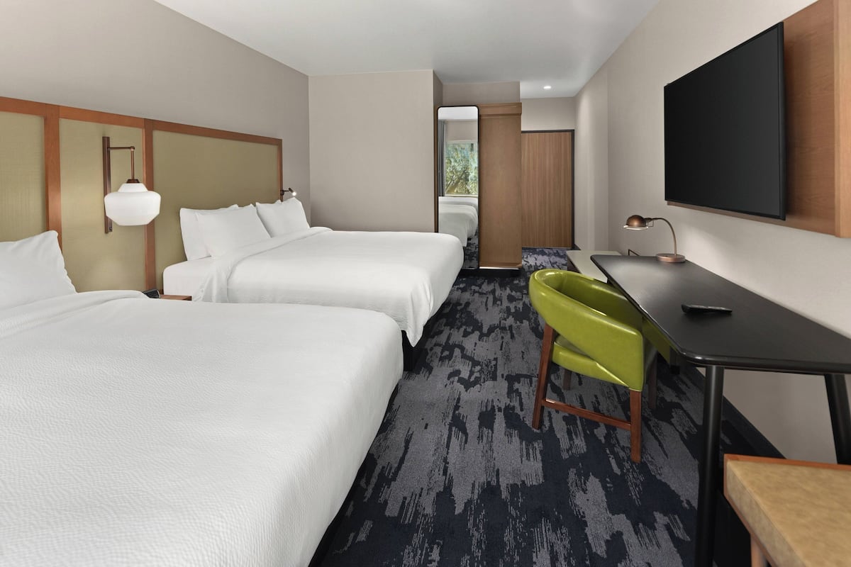 A hotel room with two beds, a desk, a chair, and a TV.
