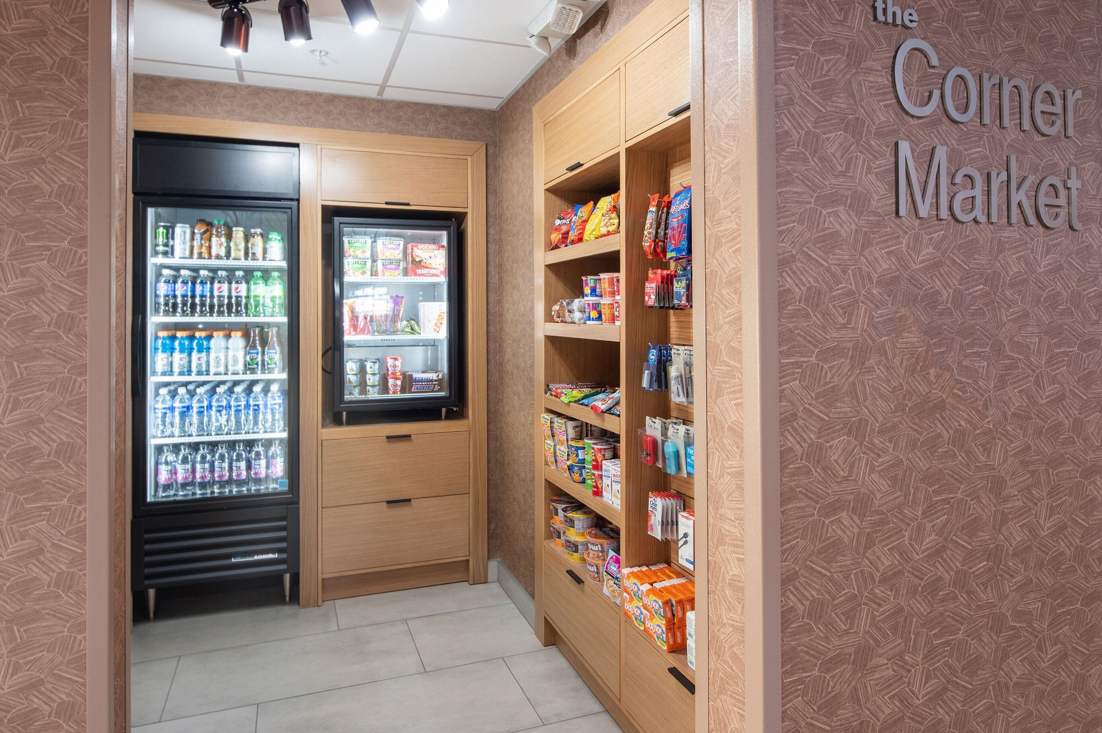 Un mercado de barrio con dispensadores de bebidas refrigeradas y estantes repletos de aperitivos y productos básicos.
