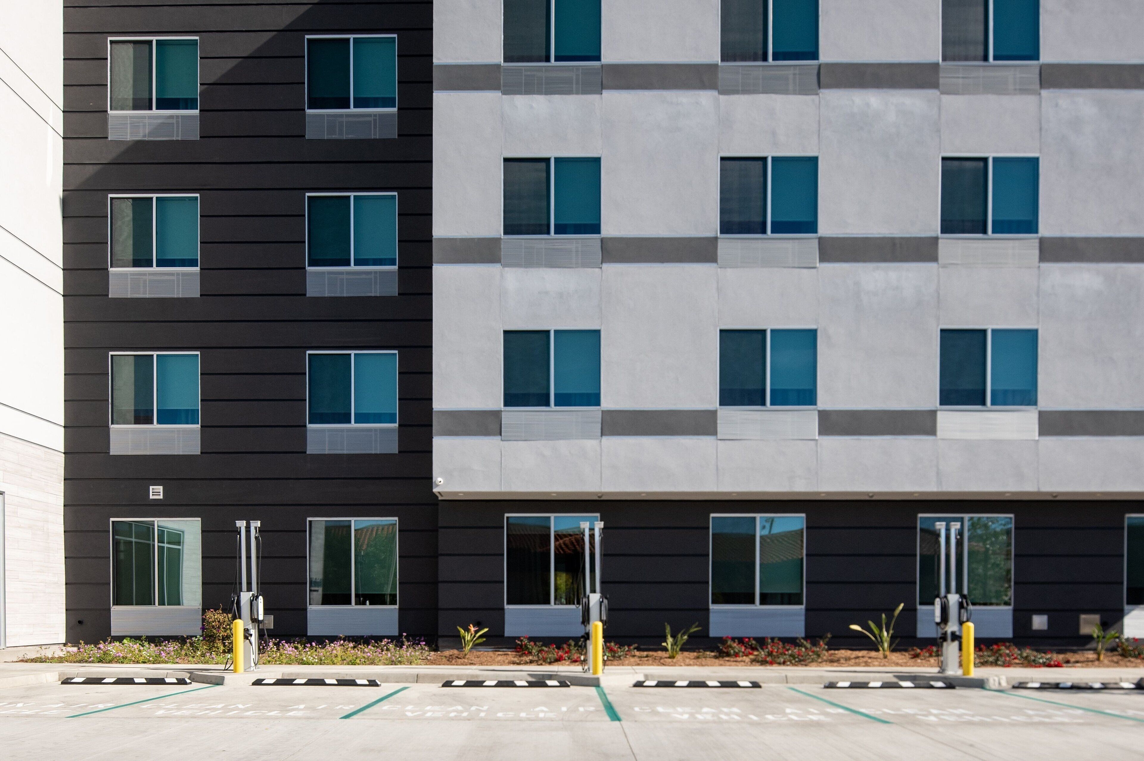 A modern building with a two-tone facade, large windows, and a parking area with marked spaces.
