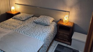 Un dormitorio con una cama, lámparas de noche, una mesita de noche, una ventana y una obra de arte colgada en la pared.