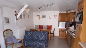 Un espacio habitable compacto con sofá, una mesa de madera, una silla y una cocina con armarios y un refrigerador.